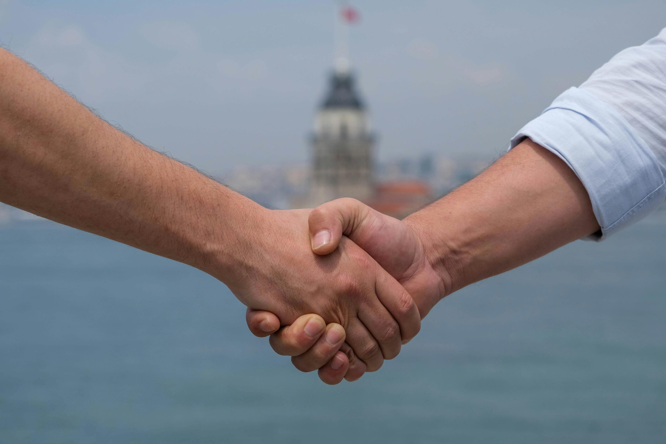 Close-up of handshake at Bosphorus with Maiden's Tower in background, symbolizing cooperation.